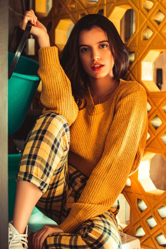 woman sitting on a cabinet wearing a yellow knit sweater and tailored trousers 