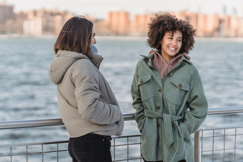 Two women in fall looks enjoying a scenic river view, with one wearing a fashionable heavy-weight shacket ideal for the transitional season