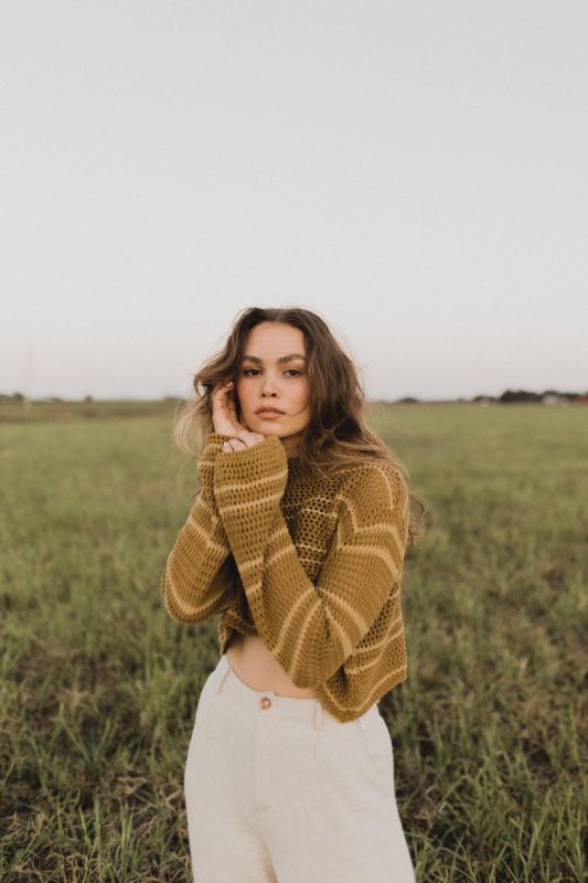woman wearing a striped knit sweater and pants outside in a green field