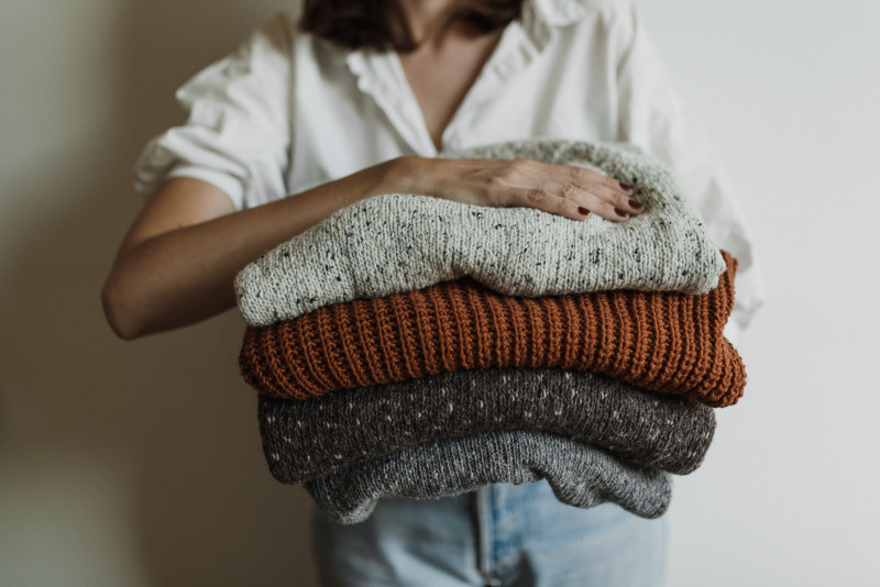 woman holding folded knit sweaters
