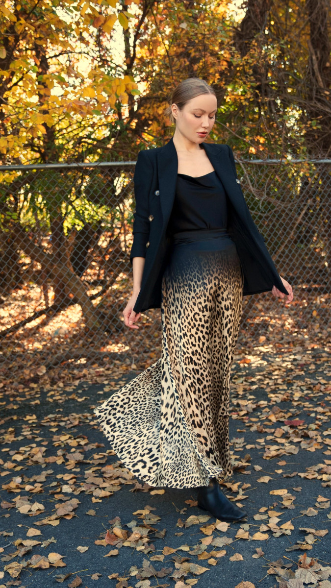 Outdoor photo of model wearing Fiera Maxi Skirt free sewing pattern from Mood Fabrics, paired with a black blazer and camisole, surrounded by autumn leaves. | Fiera Maxi Skirt Free Sewing Pattern - Leopard Printed Silk Charmeuse Fashion Fabric - Model Photo - MDF416 - Mood Fabrics Sewciety Blog