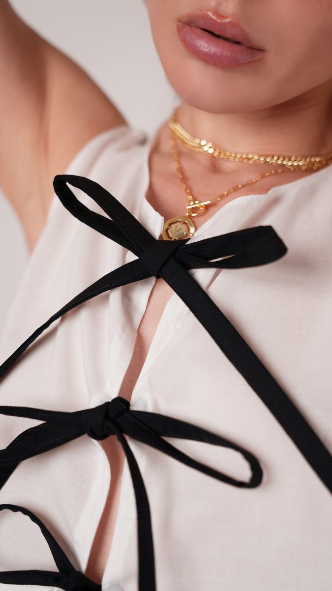 Close up view of the bow tie closure made from black cotton voile and gold jewelry