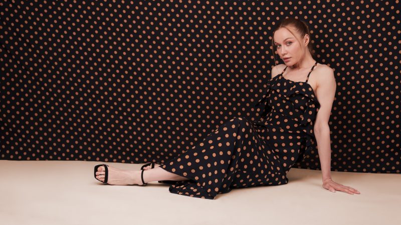Female model laying on her side with polka dot dress and matching polka dot background
