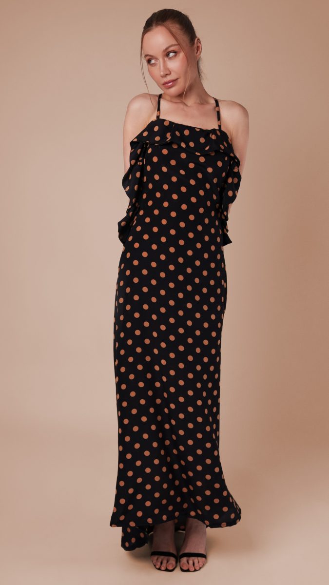 Female model posing looking to the side with her arms behind her back wearing polka dot sweep dress