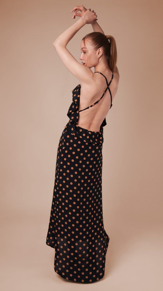 Back view of female model posing with her arms up looking to the side wearing polka dot sweep dress with ruffle and adjustable straps