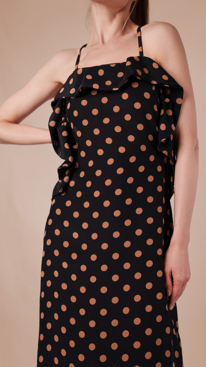 Close up view of model posing with one hand on her waist wearing polka dot dress with ruffle and spaghetti straps