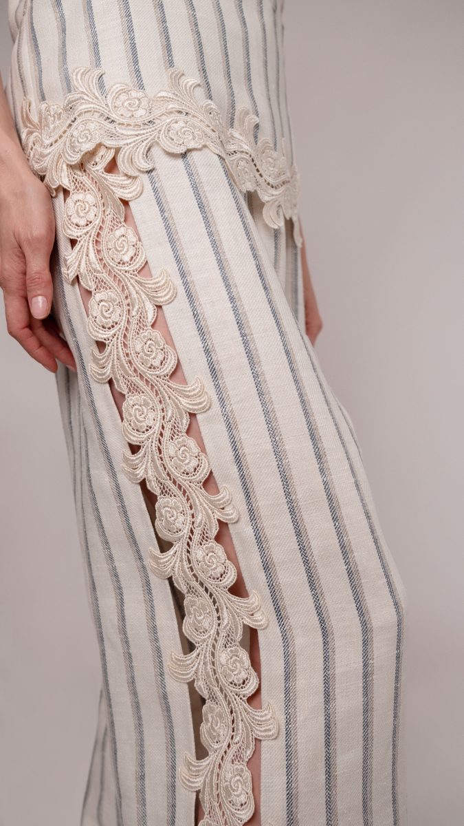 Close up side view of model posing with one leg forward wearing linen pants with venise lace trim