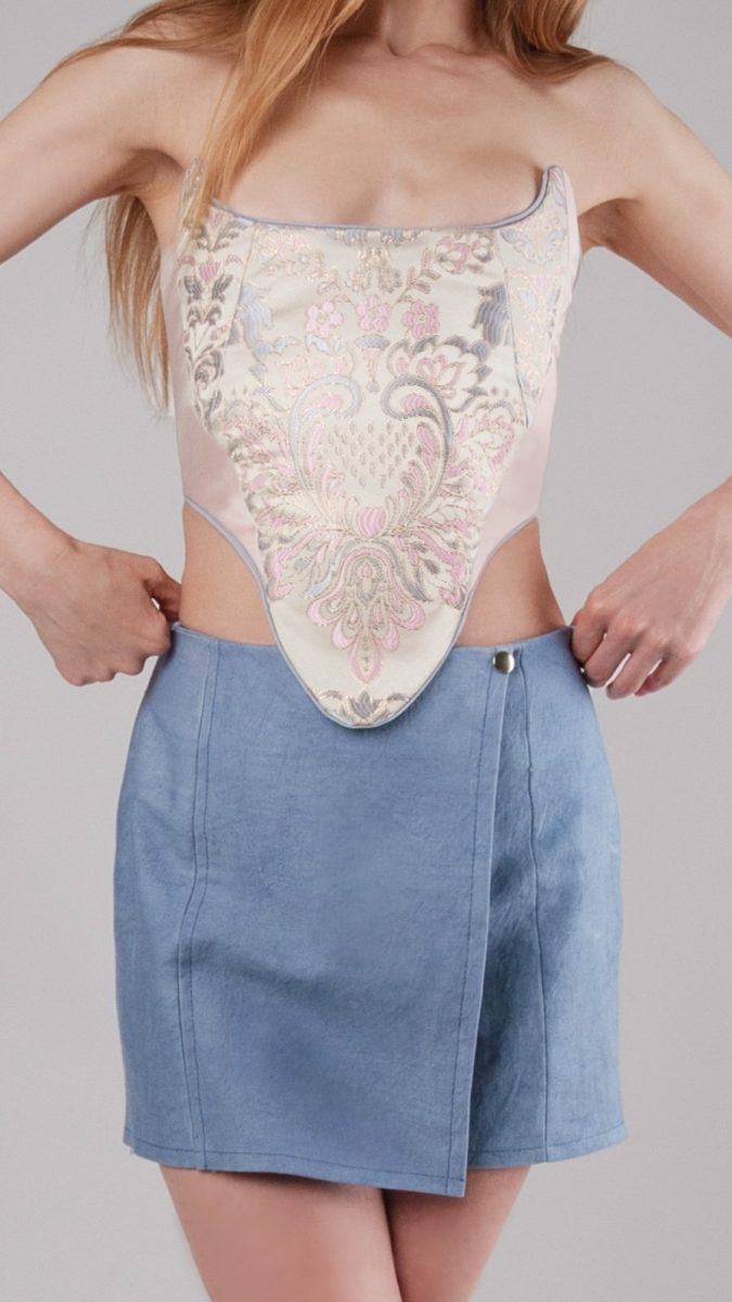Closeup front view of model wearing pink corset top & blue denim skort.