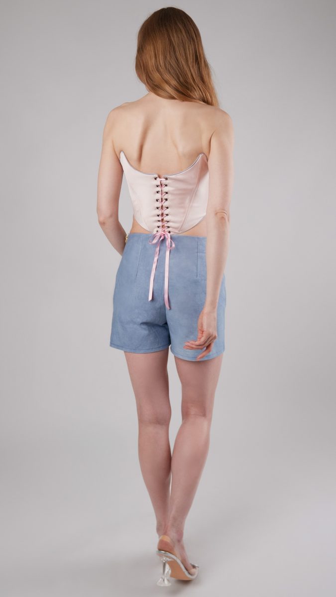 Back view of model walking wearing pink corset top and blue denim skort with heels