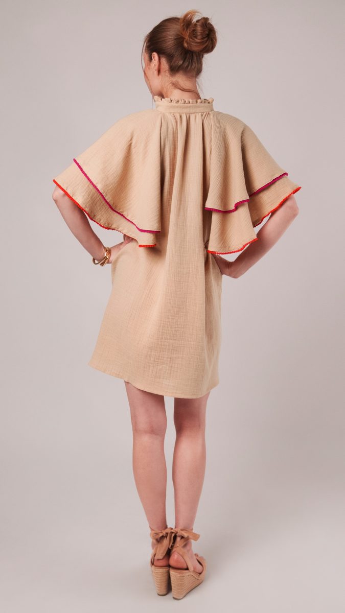 Back view of model posing with her hands on her hips wearing an A-line dress made from double cotton gauze fabric and miniature pom pom trim