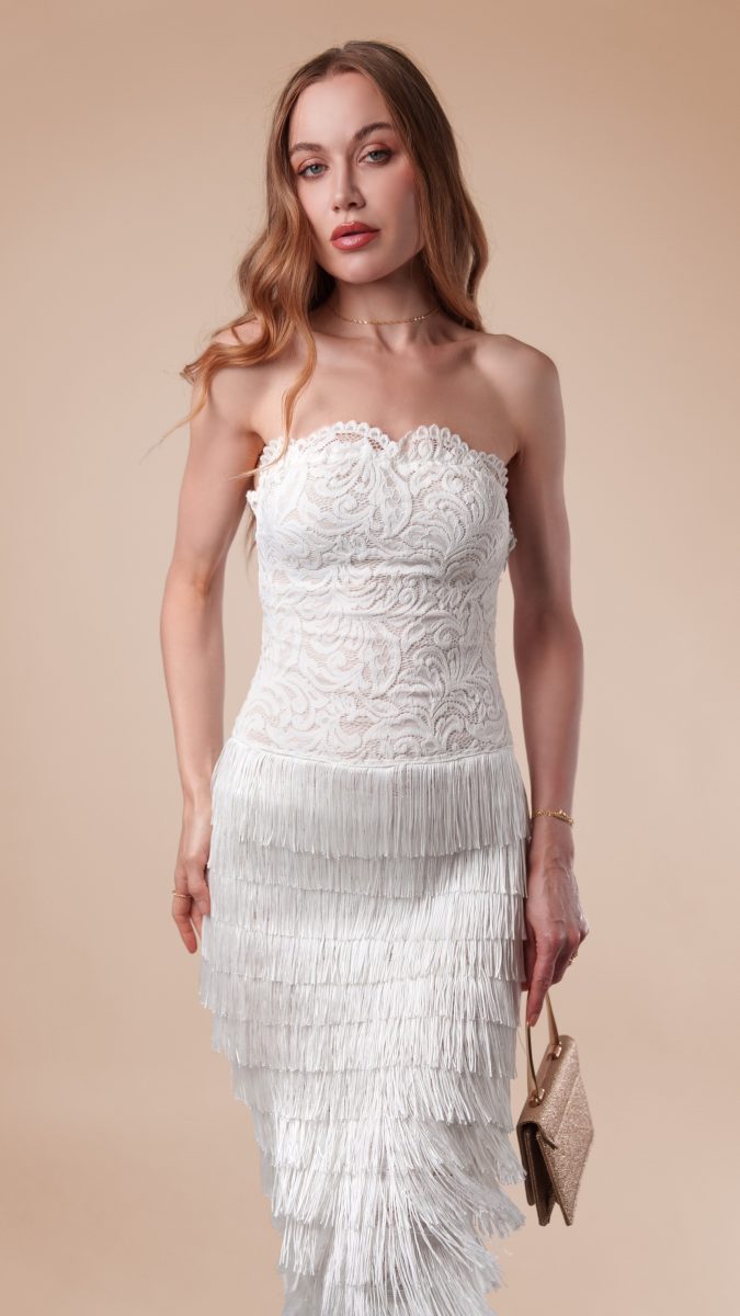 Model wearing Lumiere Strapless Dress, featuring a fitted lace bodice and layered fringe skirt, styled with a small gold handbag for a flapper-inspired 1920s look.