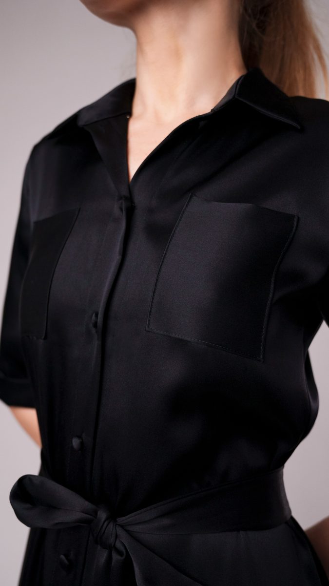 Model wearing a long Black Double-Face Silk Charmeuse 36mm Axel Shirt Dress Free Sewing Pattern by Mood Fabrics Sewicety Blog with button-down front, short sleeves, and waist tie belt styled with black heels.