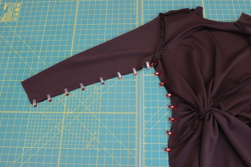 How-To-Pin-Front-and-Back-Halves-of-Dress-Together-From-Wrist-to-Hem-Dark Chocolate Stretch Polyester Crepe Knit--Mood-Fabrics Fold the dress in half and pin the front and back halves of the dress together from wrist to armpit to bottom hem.