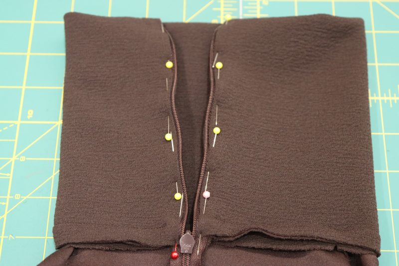 How To Fold Raw-Edges-Of-Collar-In-Towards-Zipper-Tape - Invisible Zipper 24" by YKK - 917 Dark Chocolate - Nob Hill Draped Midi Dress - MDF458 - Mood Fabrics Sewciety Blog Fold the raw edges of the collar in towards the zipper, tucking the end of the zipper tape into the collar.