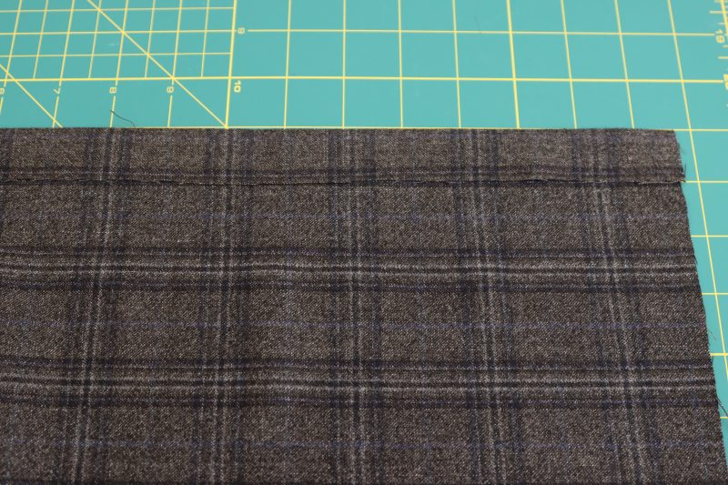 How To Iron Fold Along Bottom Edge Of Main Fabric - Super 130s Wool Twill Suiting Made in Italy Charcoal Gray Navy Plaid Deadstock - Mood Fabrics - Oxford Pleated Skirt and Tie Free Sewing Pattern Tutorial - MDF460 - Mood Fabrics Sewciety Blog - Iron a 1 inch fold along the bottom of the shell fabric.