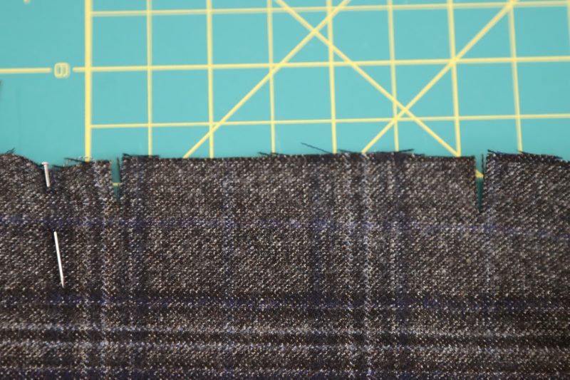 How To Match Notches Along Larger Pleat Spaces - Super 130s Wool Twill Suiting Made in Italy Charcoal Gray Navy Plaid Deadstock - Mood Fabrics - Oxford Pleated Skirt and Tie Free Sewing Pattern Tutorial - MDF460 - Mood Fabrics Sewciety Blog - Match up the two notches on either side of the larger spaces.