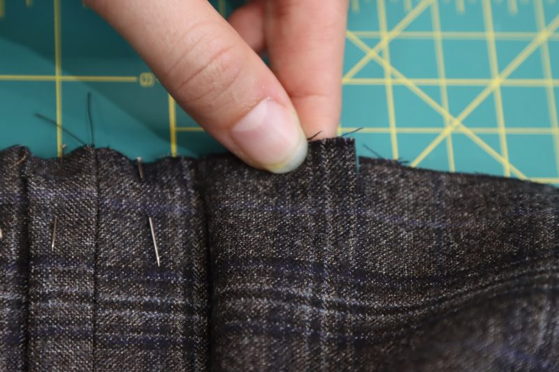 How To Fold Third Notch Flat - Super 130s Wool Twill Suiting Made in Italy Charcoal Gray Navy Plaid Deadstock - Mood Fabrics - Oxford Pleated Skirt and Tie Free Sewing Pattern Tutorial - MDF460 - Mood Fabrics Sewciety Blog - Fold the third notch on top of the first two and pin the three layers together.