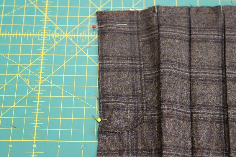 How To Pin Sew Fly Facing To Center Seam Opening - Super 130s Wool Twill Suiting Made in Italy Charcoal Gray Navy Plaid Deadstock - Mood Fabrics - Oxford Pleated Skirt and Tie Free Sewing Pattern Tutorial - MDF460 - Mood Fabrics Sewciety Blog - Pin the long flat side of the fly facing right sides together with the front center seam of the skirt.