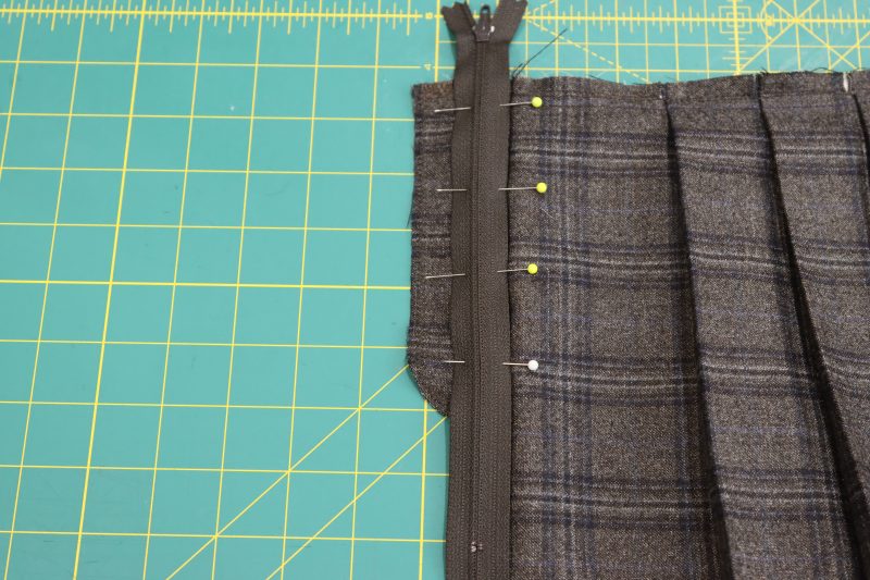 How To Pin Zipper Right Sides Together Along Center Front Seam - Regular Zipper 9 Inch YKK 916 After Dark - Mood Fabrics - Oxford Pleated Skirt and Tie Free Sewing Pattern Tutorial - MDF460 - Mood Fabrics Sewciety Blog - Pin the zipper right sides down onto the fly facing.
