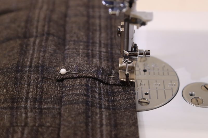 How To Sew Top and Bottom Of Belt Loops To Waistband - Super 130s Wool Twill Suiting Made in Italy Charcoal Gray Navy Plaid Deadstock - Mood Fabrics - Oxford Pleated Skirt and Tie Free Sewing Pattern Tutorial - MDF460 - Mood Fabrics Sewciety Blog - Sew the top and bottom of the belt loops to the top and bottom of the waistband.