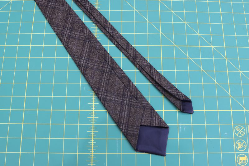 How To Fold Long Ends Of Tie Inward - Super 130s Wool Twill Suiting Made in Italy Charcoal Gray Navy Plaid Deadstock - Mood Fabrics - Oxford Pleated Skirt and Tie Free Sewing Pattern Tutorial - MDF460 - Mood Fabrics Sewciety Blog - Fold both long ends of the tie inwards towards the center and iron flat.