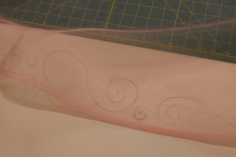 How To Paint Glitter Onto Ruffles - Satin Faced Organza - Mood Fabrics - Glinda Gown Free Sewing Pattern Tutorial - MDF463 - Mood Fabrics Sewciety Blog - Hand paint sparkly bubbles and swirls on the outer edge of the ruffle pieces with the horsehair braid.