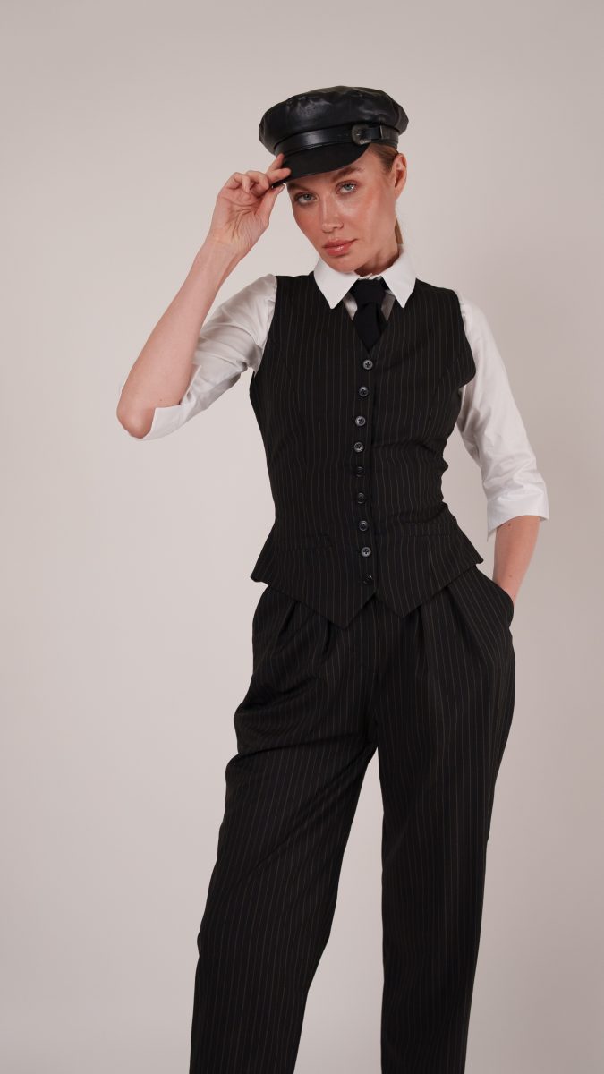 Close-up of model in the Anne Waistcoat Ensemble, tipping a black leather cap while showcasing sharp tailoring and 1920s gangster style.