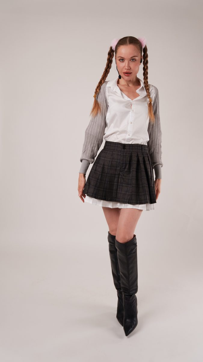 Woman in a white button-down blouse with gray sleeves, pleated plaid mini skirt, and knee-high boots, styled as a Britney Spears schoolgirl costume idea using the Oxford Skirt sewing pattern.