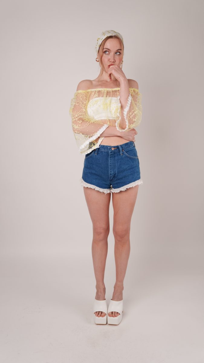 Model wearing the Juno Top, a yellow puff-sleeve cropped blouse with lace details paired with denim shorts — Sabrina Carpenter-inspired costume idea.