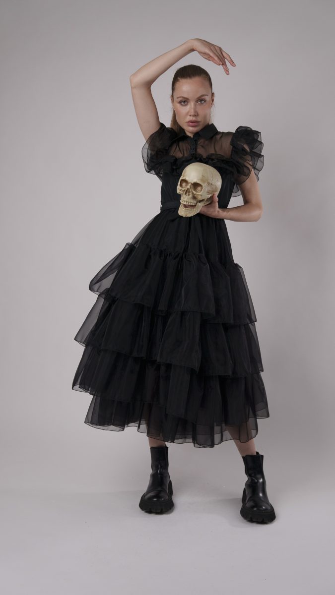 Model in black Nightshade gothic dress with tiered tulle skirt, holding a skull prop for a dramatic Halloween costume look.