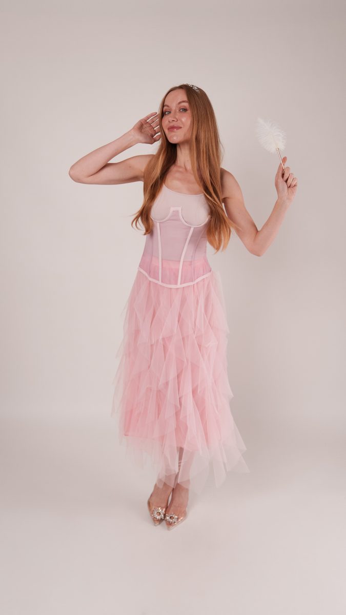 Model wears the Roslyn Ruffled Midi Skirt and Parker Corset in soft pink, styled with a tiara and feather wand for a Glinda-inspired Halloween costume.