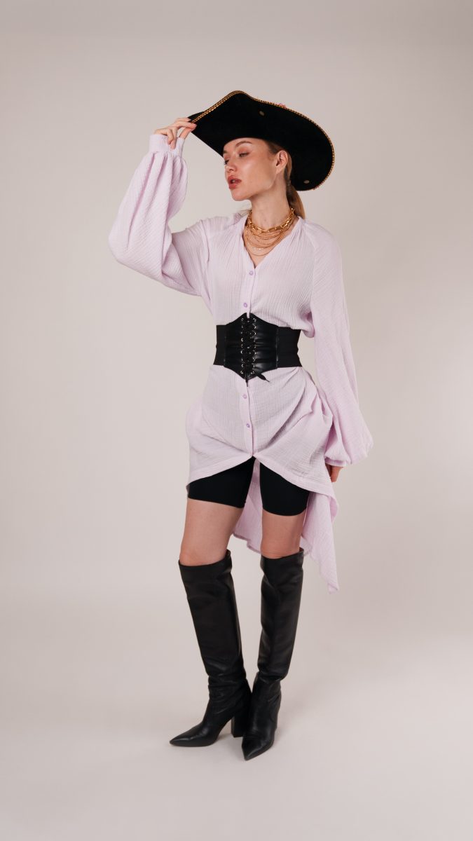 Model strikes a pose in the pirate look, showcasing the flowing gauze fabric of the Tundra Dress with button-front detail, corset belt, and tall boots.