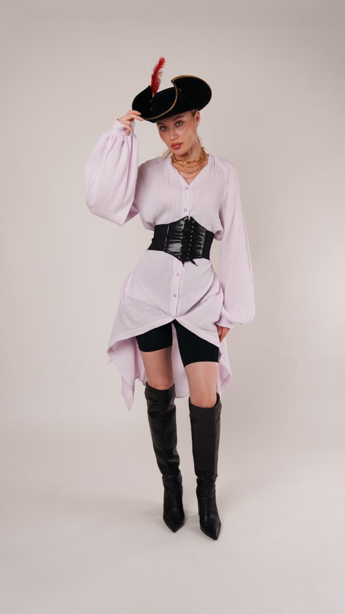 Woman in a lilac button-down high-low dress with corset belt, thigh-high boots, and tricorn pirate hat, styled as a Pirate Halloween costume idea using the Tundra Dress sewing pattern.