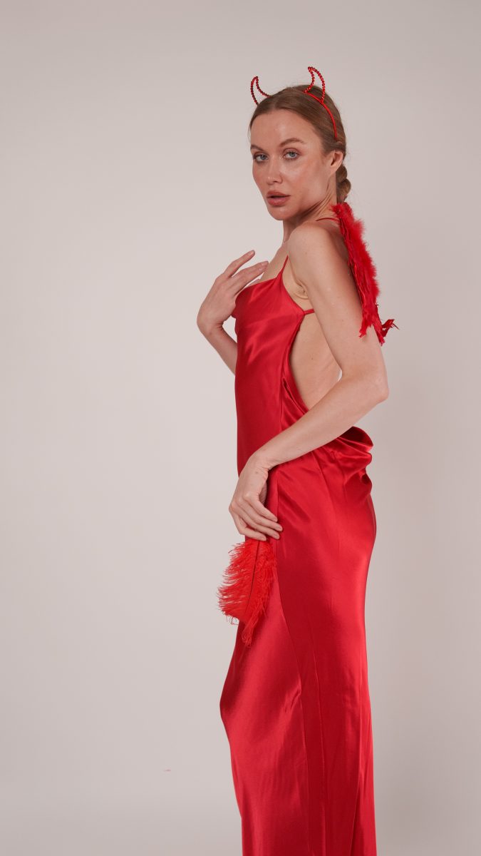 Side view of the Vixen Slip Dress devil costume, featuring a sleek red satin silhouette, feather wings, and devil horn headband for a bold Halloween look.