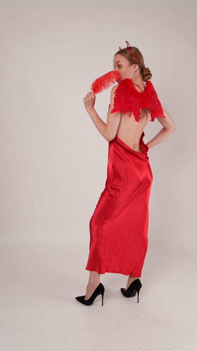 Back view of the devil costume in the Vixen Slip Dress, showing feathered wings, red horns, and playful pose with a red feather accessory.