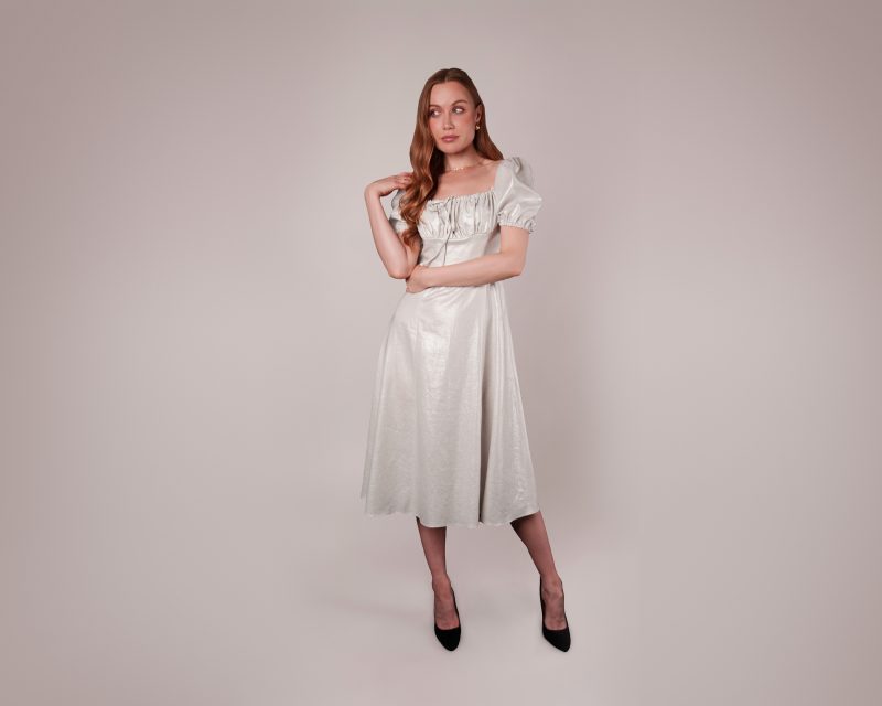 A model wearing a light metallic silver midi-length Anthea Milkmaid Dress (MDF317), featuring a sweet heart neckline, short puff sleeves, and a shirred bust detail.