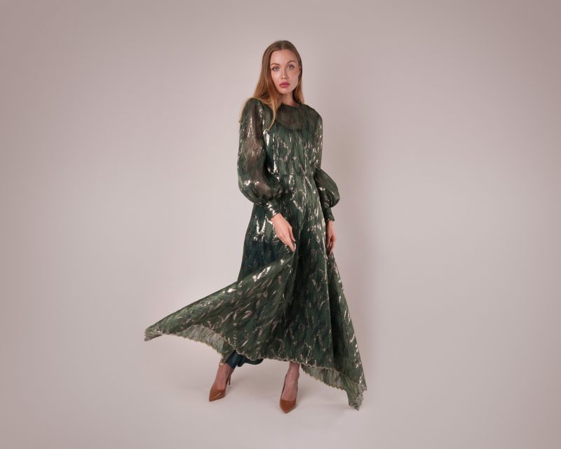 A model wearing the shimmering green sequin Harper Plisse Dress (MDF404), a maxi-length gown with long, voluminous blouson sleeves and a flowy, high-neck design.