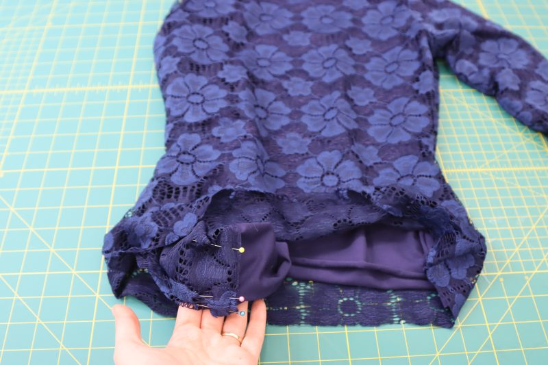 How To Pull Sleeves Through Hem - Stretch Crochet Lace - Mood Fabrics - Altena Blouse Free Sewing Pattern Tutorial - MDF491 - Mood Fabrics Sewciety Blog - Pull the ends of the sleeves out through the bottom hem of the shirt then pin.