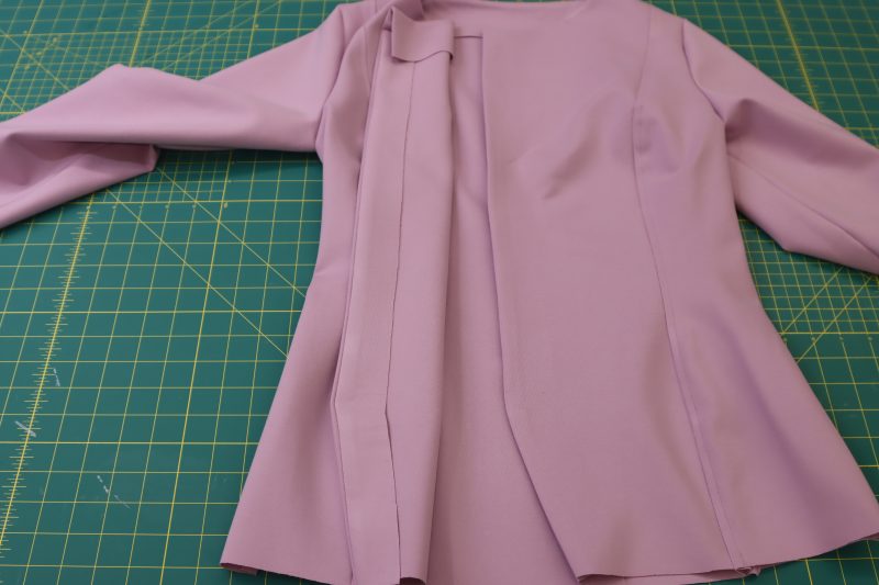 How To Flip Placket Facings Inside Cardigan - Stretch Ponte Knit - Mood Fabrics - Camarillo Cardigan and Magdalene Midi Skirt Free Sewing Pattern Tutorial - MDF490 - Mood Fabrics Sewciety Blog - Flip the button placket facing so that it is wrong sides together with the front of the jacket. Iron the center front seams so that the facing is hidden from the outside.