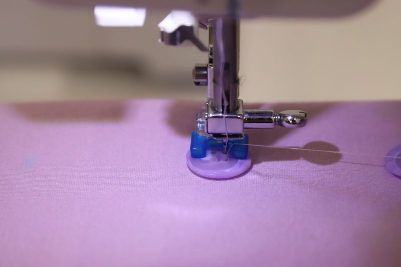 How To Line Up Button With Preser Foot - Lilac Swirl Buttons - Mood Fabrics - Camarillo Cardigan and Magdalene Midi Skirt Free Sewing Pattern Tutorial - MDF490 - Mood Fabrics Sewciety Blog - Line up the button holes with the needle and put the presser foot down to hold it in place.