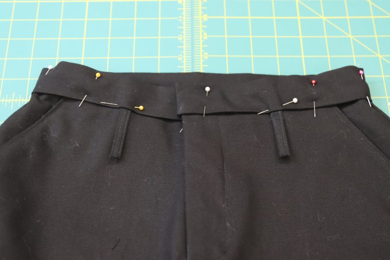 How To Pin Waistband To Waistline - Cotton Canvas - Mood Fabrics - Clarkston Carpenter Pants Free Sewing Pattern Tutorial - MDF503 - Mood Fabrics Sewciety Blog - Pin the waistline of the pants into the waistband with the belt loops.