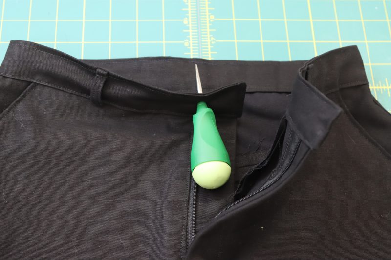 How To Insert Hole Into Waistband - Cotton Canvas - Mood Fabrics - Clarkston Carpenter Pants Free Sewing Pattern Tutorial - MDF503 - Mood Fabrics Sewciety Blog - Poke a hole through the waistband with an awl.