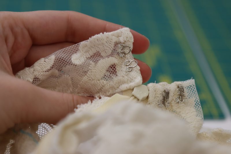 How To Sew Eye By Hand - Hooks And Eyes - Mood Fabrics - Taiga Trapeze Skirt Free Sewing Pattern Tutorial - MDF512 - Mood Fabrics Sewciety Blog - Hand sew the “eye” pieces of the hooks and eyes to the inside of the waistband.
