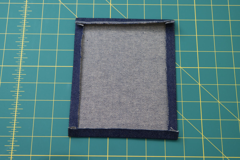 How To Fold Back Pocket Edges Folded And Pressed Wrong Side - Cotton Denim Twill - Mood Fabrics - Merit Jumpsuit Free Sewing Pattern Tutorial - MDF525 - Mood Fabrics Sewciety Blog - Fold and press the edges of the back pockets toward the wrong side of the fabric.
