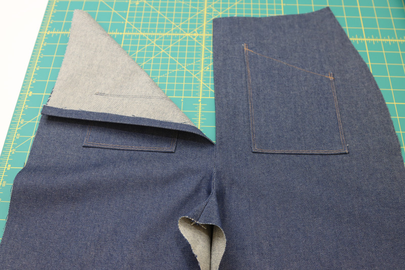 How To Press Front Crotch Raw Edges Folded Inside - Cotton Denim Twill - Mood Fabrics - Merit Jumpsuit Free Sewing Pattern Tutorial - MDF525 - Mood Fabrics Sewciety Blog - Press the rest of the seam above the front crotch seam so that the raw edges are folded toward the inside of the pants.