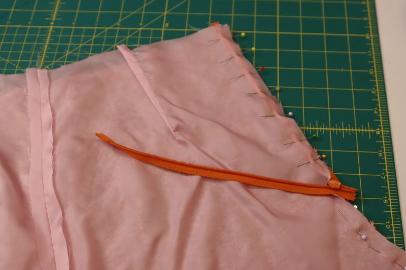 How To Pin Zipper Tape Between Lining And Sequined Fabric At Back Crotch Seam - Invisible Zipper - Mood Fabrics - Morganite Waistcoat Ensemble Free Sewing Pattern Tutorial - MDF519 - Mood Fabrics Sewciety Blog - Pin the zipper tape between the lining and the sequined fabric at the back crotch seam.