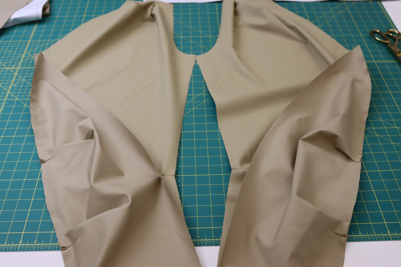 How To Pin Sew Pleated Sides Of Front Pants Panels To Cutout At Bottom Of Front Pants Pieces - Stretch Khaki Twill - Mood Fabrics - Lucca Tailored Barrel Leg Pants Free Sewing Pattern Tutorial - MDF524 - Mood Fabrics Sewciety Blog - Pin and sew the pleated sides of the front pants panels to the cutout at the bottom of the front pants pieces.