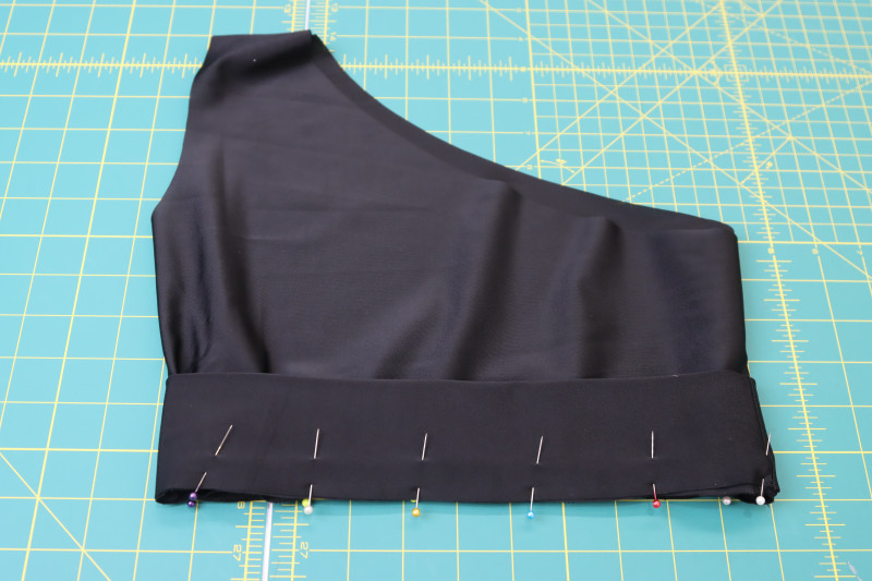 How To Pin Waistband Right Sides Together With Raw Edge Of Bikini Top - Recycled Swimwear Tricot - Mood Fabrics - Antikythera One Shoulder Bikini Free Sewing Pattern Tutorial - MDF531 - Mood Fabrics Sewciety Blog - Pin the waistband right sides together with the raw edge of the bikini top.