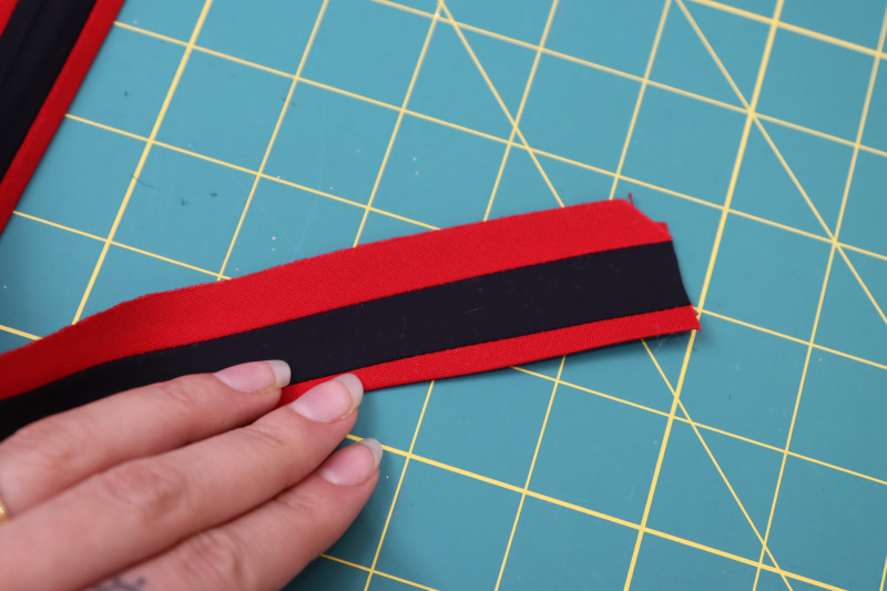 How To Press Bias Tape Raw Edges - Red Quilting Cotton - Mood Fabrics - Matrix Shawl Collar Ensemble Free Sewing Pattern Tutorial - MDF543 - Mood Fabrics Sewciety Blog - Press the raw edges of the bias tape toward the wrong side of the trim.