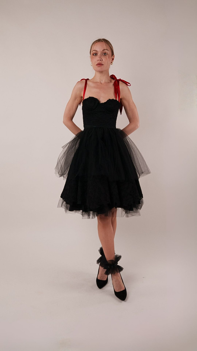 A model wearing the Parker Corset Redux, featuring a black lace bustier bodice with red silk ribbon shoulder straps paired with a voluminous tulle skirt.
